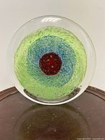 Front view of circular Murano glass paperweight showing green/blue swirl and red centre