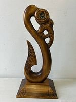 Full view of carved wood Hei Matau sculpture on stand
