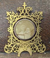 Front view showing ornate pierced brass frame, celluloid-covered circular photo opening with portrait