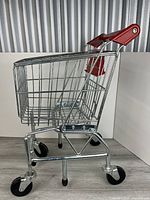 Side view of metal toy shopping cart showing basket, handle, wheels
