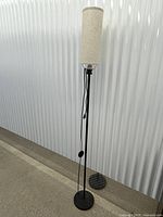 Full view of tall slim black floor lamp with beige shade