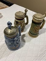 All three Avon steins side by side showing overall designs and lids