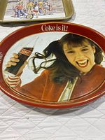 Oval red Coke is it tray foreground; portion of other tray visible