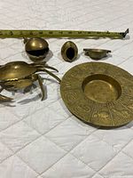 Five brass ashtrays laid out with measuring tape for scale