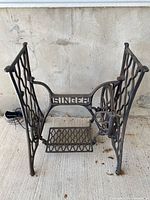 Full view of cast iron Singer treadle base showing sides, pedal, and flywheel