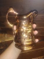 Front view of copper lusterware pitcher held in hand showing size and reflective glaze