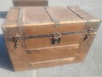 Front view of wooden steamer trunk showing metal panels, ornate hardware, central lock, side latches
