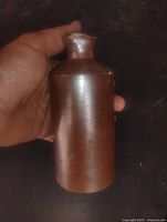 Full view of brown stoneware ink bottle held in hand