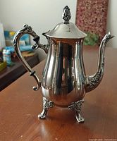 Full view of silver-plated teapot showing body, spout, handle, feet