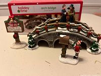 Full view of resin arch bridge, signpost, couple figurine, Santa and child figurine with box in background