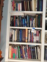 Bookshelf with three shelves densely packed with assorted hardcover books of various sizes and subjects