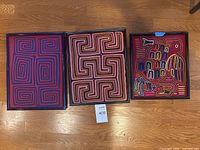 Three framed molas on floor showing size comparison and lot tag