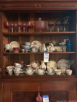 Entire cabinet shelf showing cranberry glasses, teacups, figurines and dishes