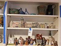 Full view of three shelves showing pottery on top, row of ceramic buildings middle, larger buildings and figurines bottom