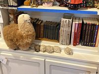 Shelf with plush alpaca, small felt figures, row of antique books, ceramic birch-style vase