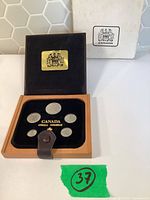 Open wood case with six coins, plaque, outer sleeve visible