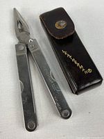 Multitool closed alongside leather pouch showing logo