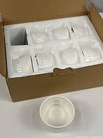 Box containing eight white ceramic ramekins seated in foam insert, one ramekin displayed separately