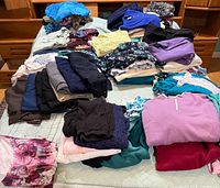 Wide view of folded women’s clothing piles on bed