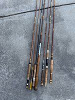 Eight vintage fishing rods laid side-by-side showing full length and grips
