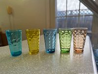 Five differently colored pressed glass tumblers on countertop