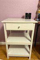 Front view of white end table showing drawer and two shelves