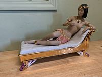 Front view of porcelain Egyptian woman figurine on gold-trimmed chaise lounge