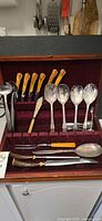 Overview of case interior showing steak knives, serving spoons, ladle, fish server, carving set and extra spoon