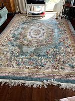Full view of ornate teal and cream floral area rug on wood floor