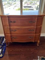 Front view of three-drawer wooden dresser with ornate pulls and curved front