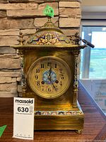 Front view of brass mantle clock showing dial, enamel decoration, key and height tag