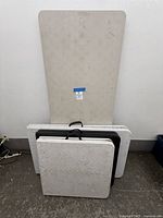 Front view showing one beige rectangular folding table and three stacked square folding tables