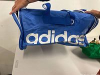 Left side view of blue Adidas duffel bag showing logo and carry handles