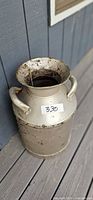 Front view of metal milk can showing handles, lid, rust and paint wear