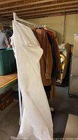 Garment rack with multiple jackets draped, white garment bag partially covering view