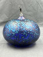 Front view showing shape, blue iridescent mottled surface, wick at top