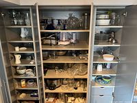 Overview of open pantry cabinets showing breadth of glassware, appliances, dishware and bakeware included
