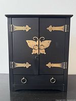 Full front view of black jewelry cabinet with brass butterfly hardware