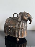 Front angled view of brass elephant box showing overall form, latch, loop handle, feet, patina