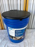 Overall view of blue bucket toilet with black seat/lid