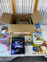 Open cardboard box filled with books, several laid out in front