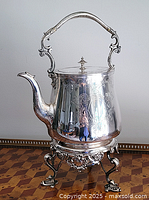 Front view of silver-plated tea kettle on ornate stand