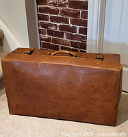Front view of brown leather suitcase showing buckle straps and handle