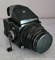 Front-left view of camera showing body, lens with cap, prism finder, crank