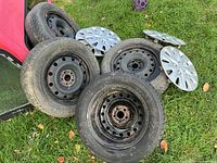 Group of four mounted tires on steel rims with four hubcaps on grass