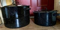 Both black speckled enamel canning kettles side by side with lids on