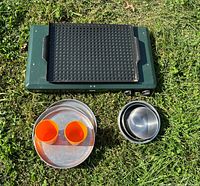 Closed Coleman stove with grill topper, plates, bowls, cups