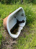 Bathtub on its side showing interior enamel and attached faucet, grass surroundings
