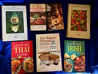 Seven cookbooks on blue cloth including Asian, Hungarian, Latin American, Thai, Irish and baking titles