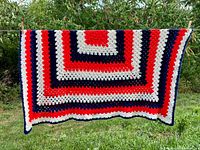 Full view of crocheted red, off-white and navy afghan hanging outdoors